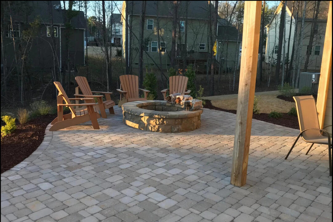 A professionally installed tan paver patio with a round stone fire pit, built under a walkout basement deck to create a functional outdoor space. Designed with Dimensions Antiqued Pavers for a timeless look and lasting durability.