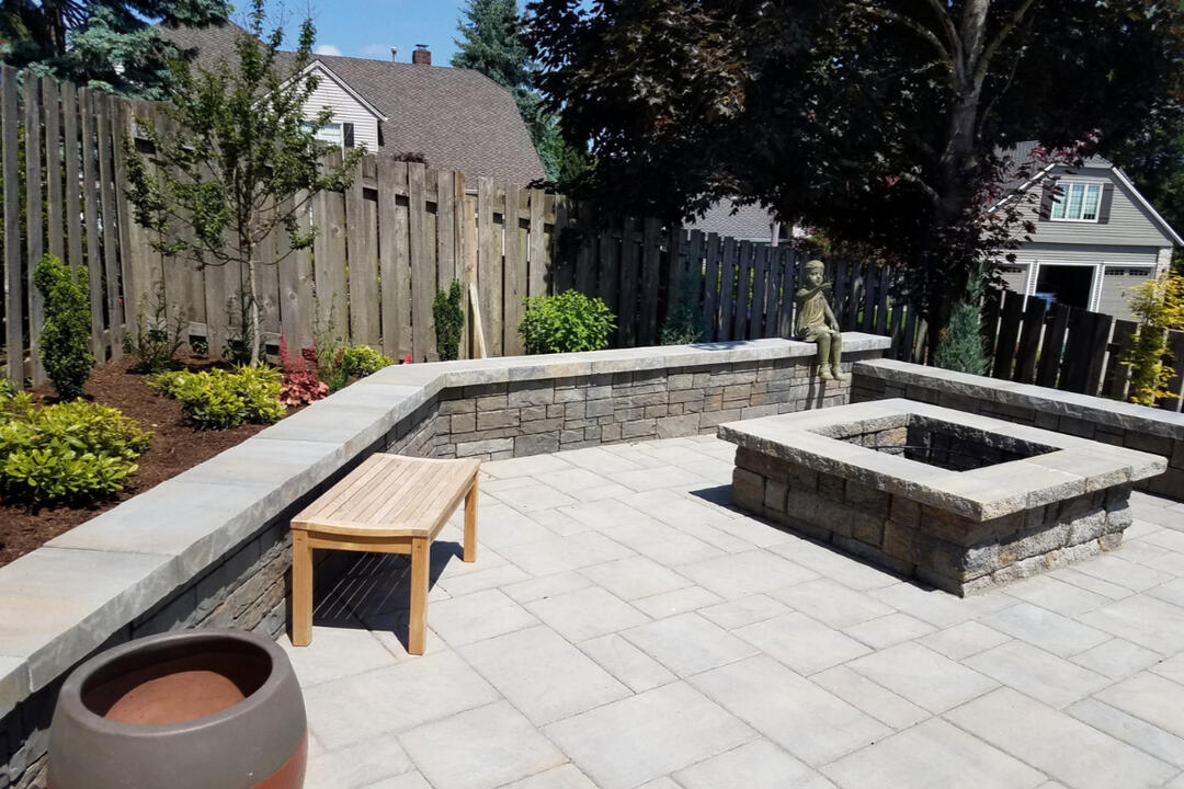New Berlin backyard patio with Ashlar Tandem Pewter retaining wall, square stone fire pit, and custom sand-silt stone capping for a cozy and inviting outdoor space.